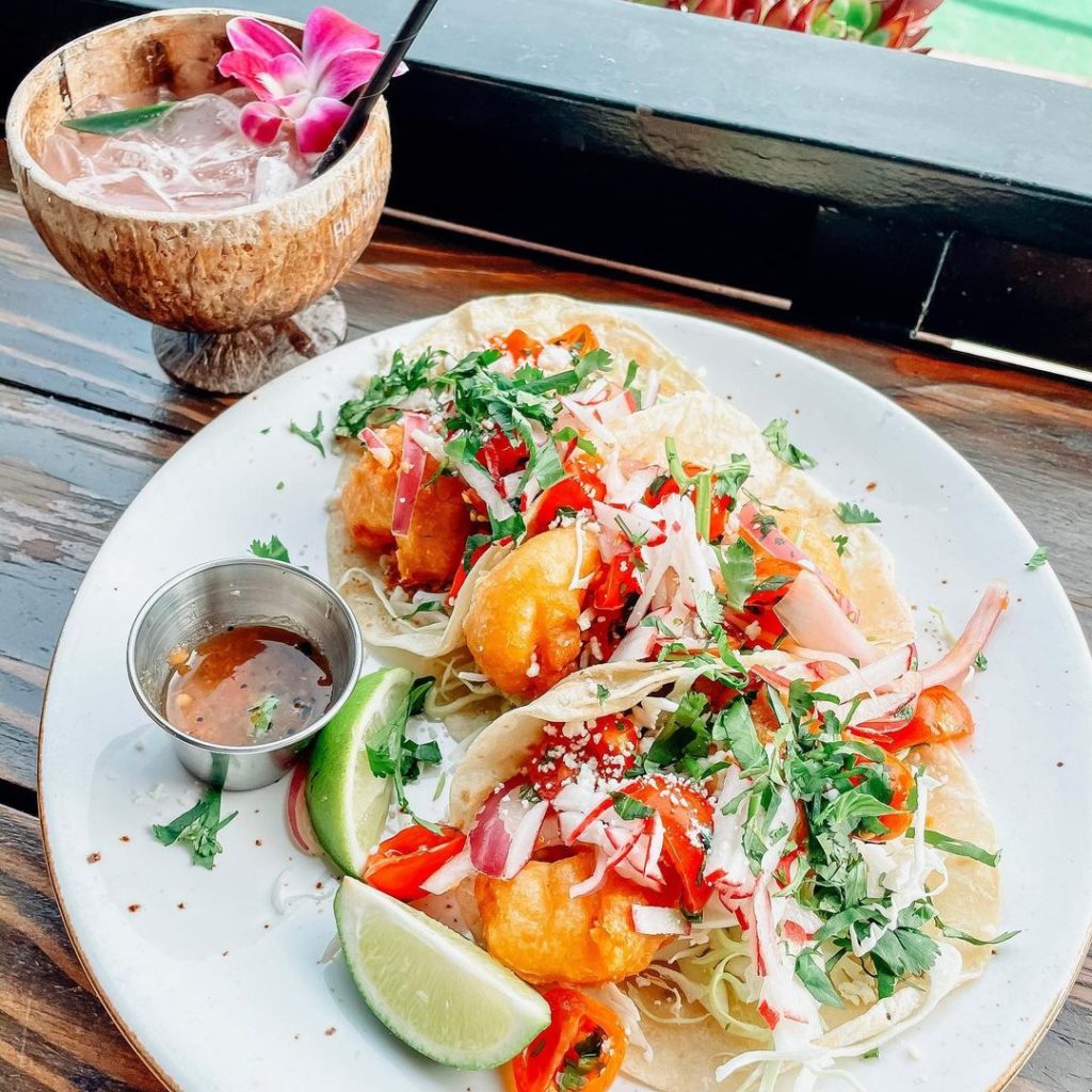 Plate of shrimp tacos on a wooden table with a wooden cocktail glass