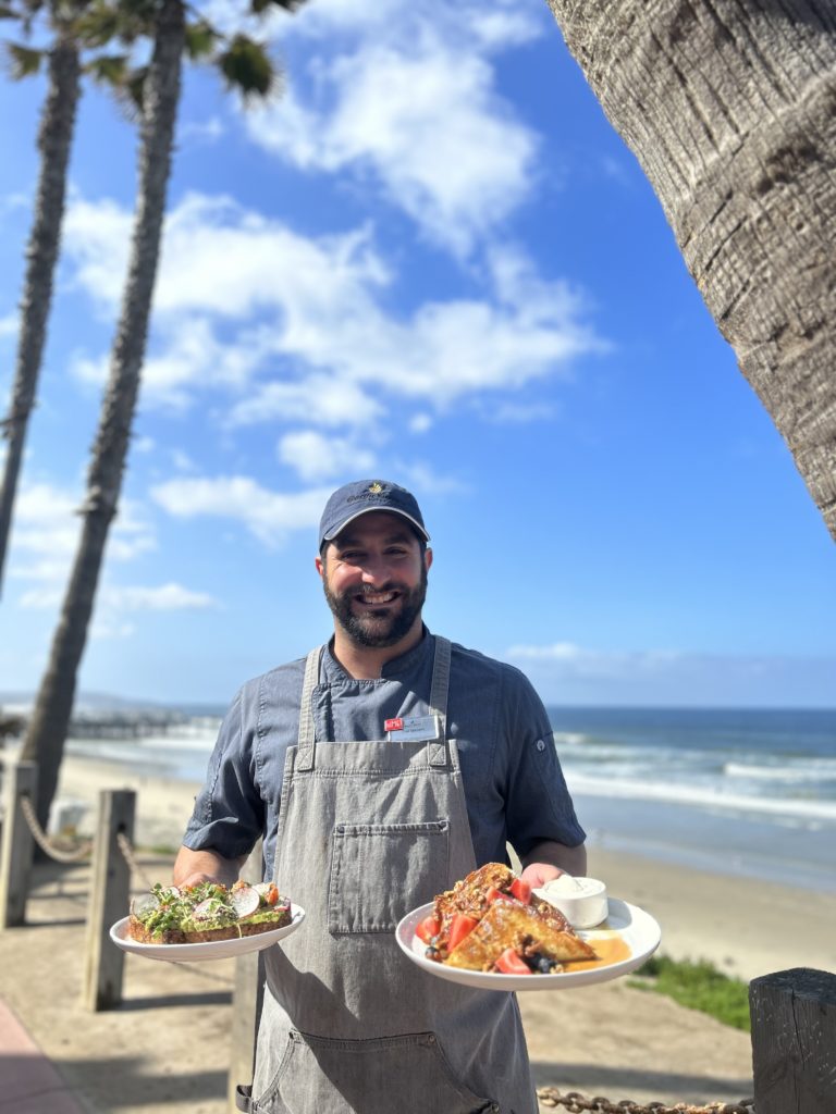 Chef holding breakfast plates with ocean behind him