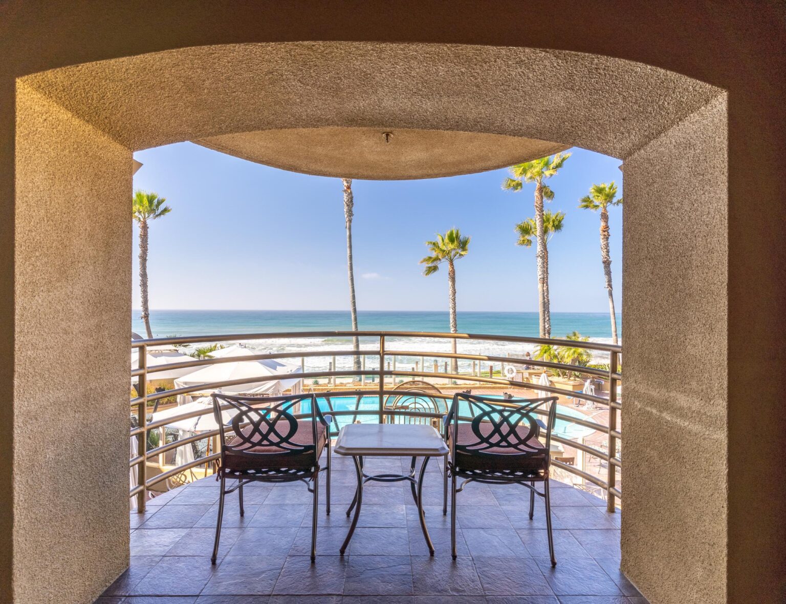 Balcony with a view of tall trees, pool, and pacific beach