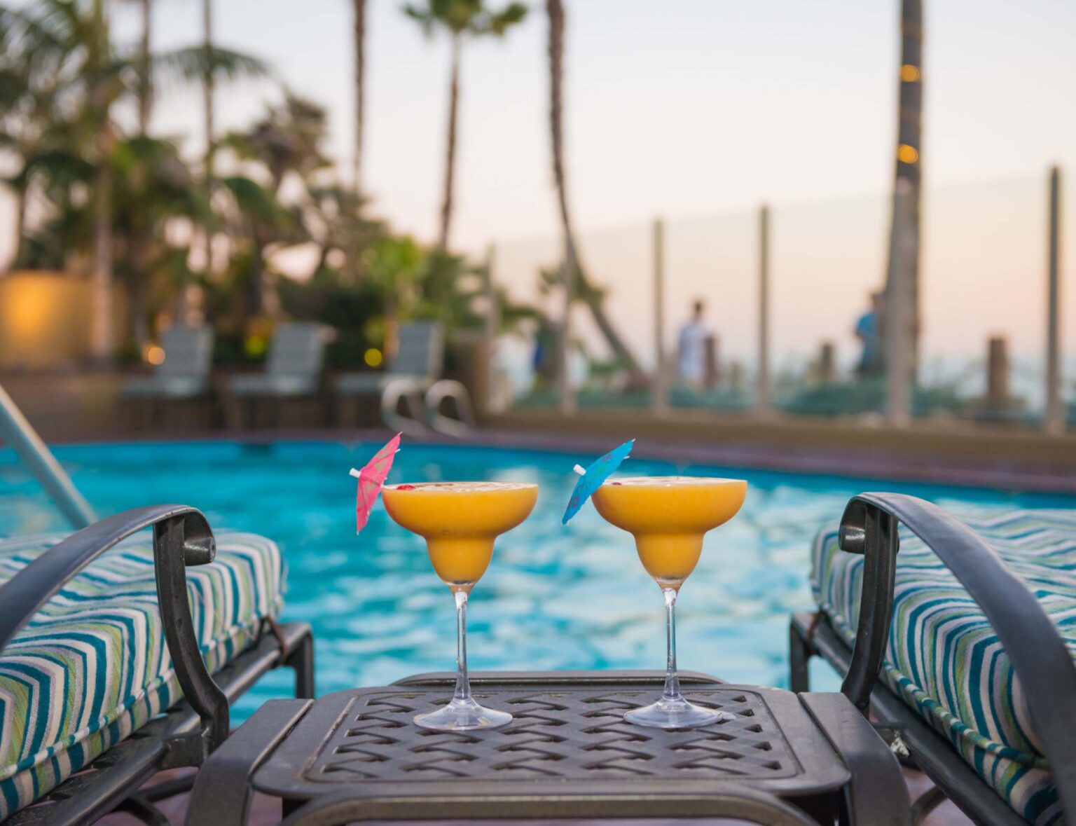 Two yellow cocktails next to two chairs with the pool and sky background