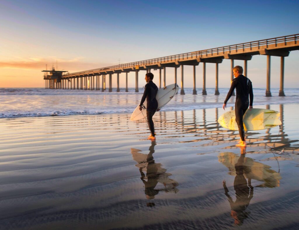 Two men walking with a surf board
