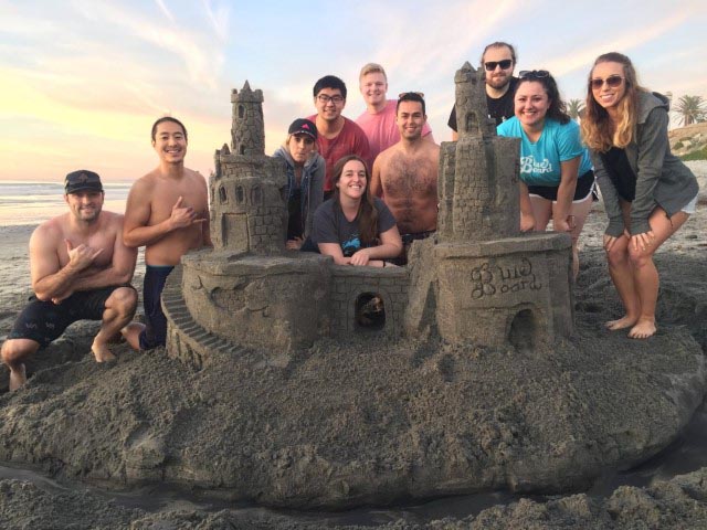People smiling next to a sand castle