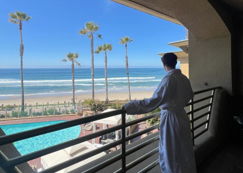 a man looking out at the beach from his hotel balcony
