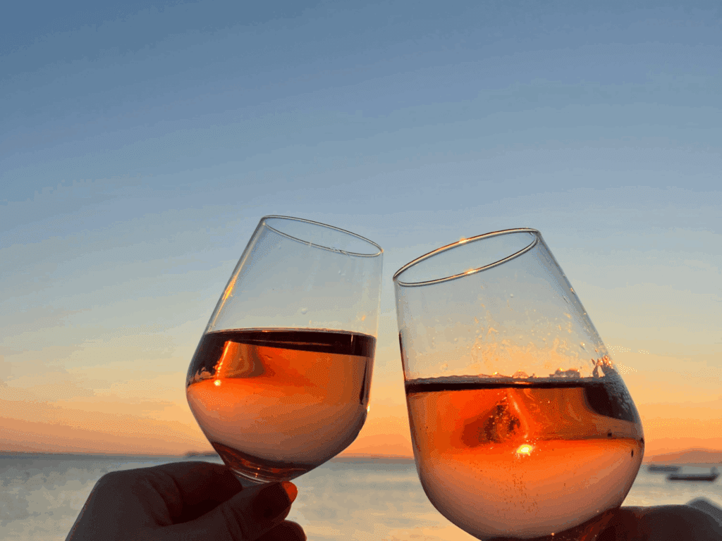 two wine glasses with sunset and ocean in background