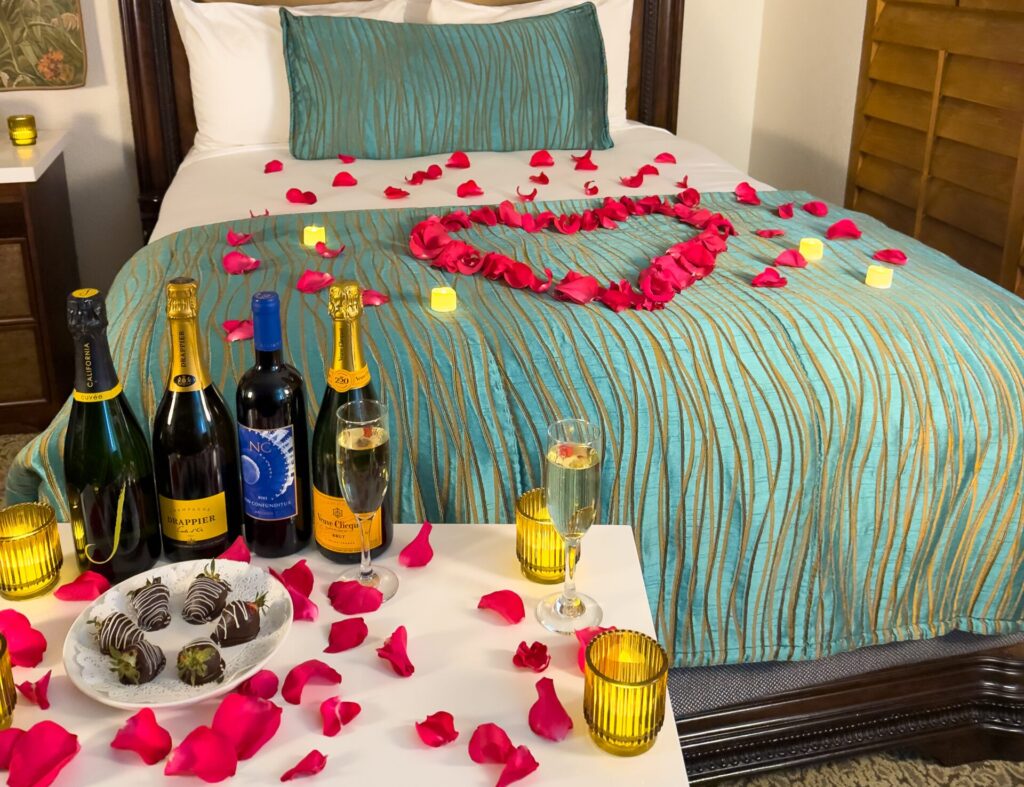 roses on bed with champagne and chocolate covered strawberries