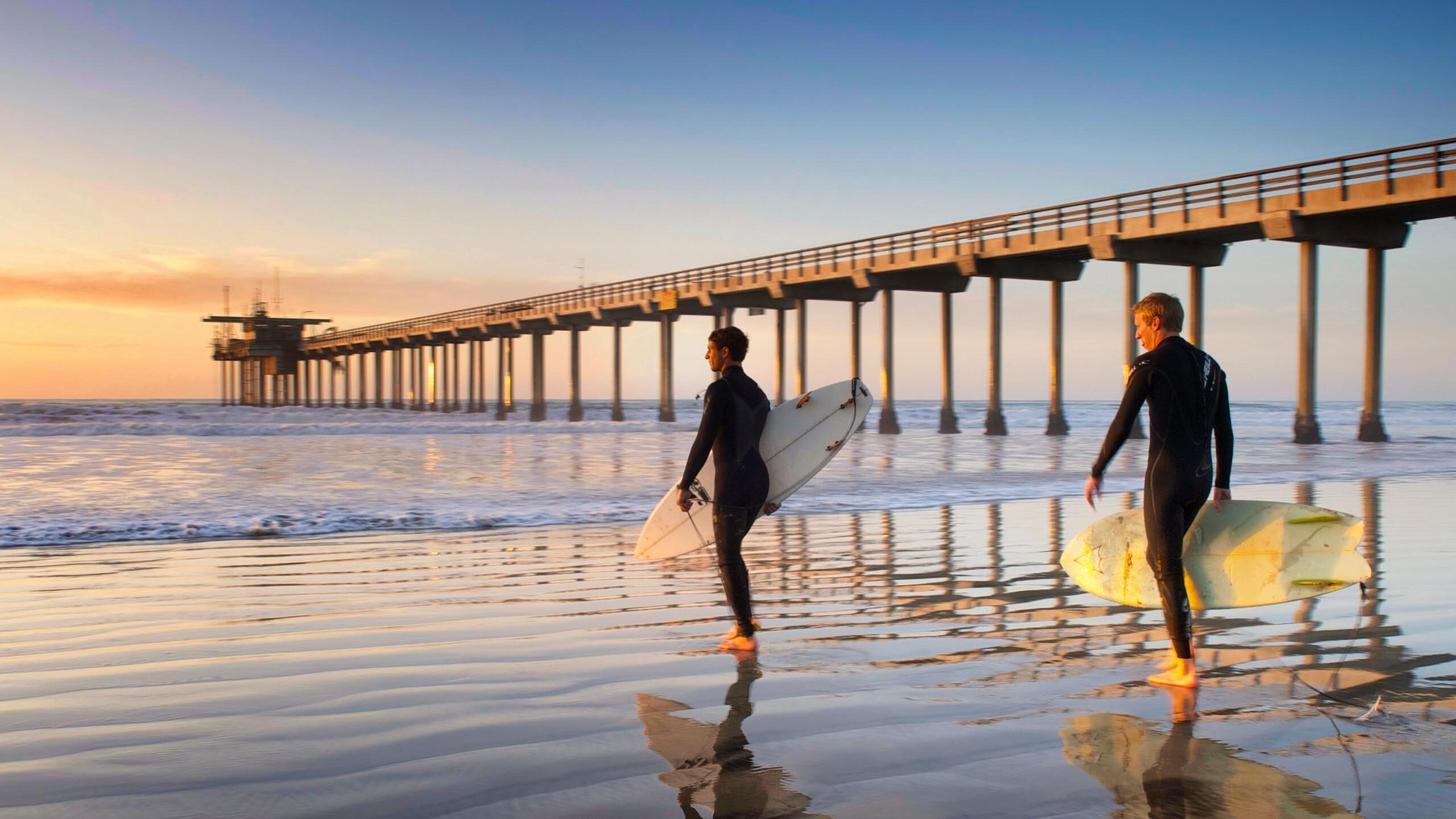Two men walking with a surf board