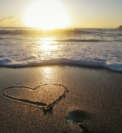 a heart drawn in the sand at sunset