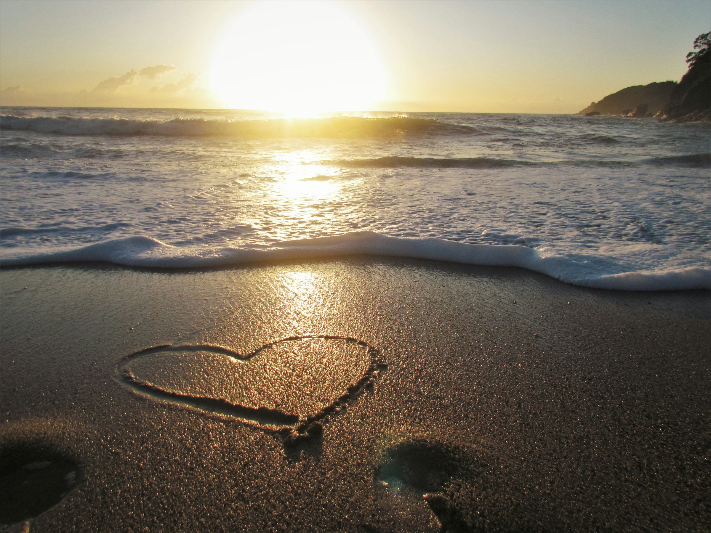 a heart drawn in the sand at sunset
